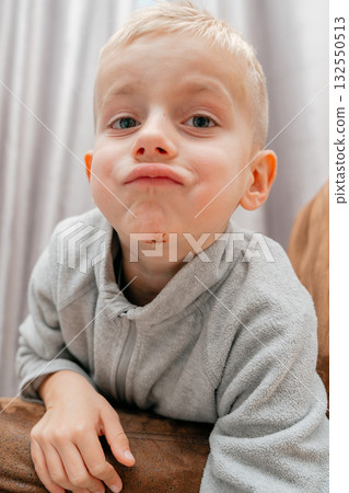 Boy looks up through light fabric, soft expression and visible chin mark intimate candid moment in calm atmosphere 132550513