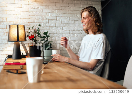 Young man enjoying a cozy workspace with a warm drink and plants in a bright room 132550649