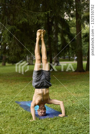 A Man is Skillfully Practicing Handstand Yoga in a Beautiful and Serene Park Setting A Man is Skillfully Practicing Handstand Yoga in a Beautiful and Serene Park Setting 132550782