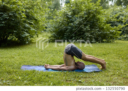 A man is practicing a yoga pose in a calm and serene natural setting surrounded by greenery 132550790