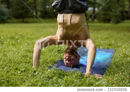 Practicing the Upside Down Yoga Pose on a Mat in a Beautiful Green Park Among Nature 132550830