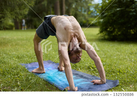 A Flexible Male is Engaging in Yoga Practice While Surrounded by the Beauty of Nature 132550886