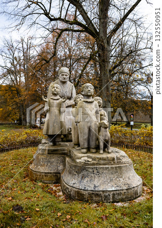 A stone statue depicting a grandmother and her grandchildren stands in Granny Valley, Ratiborice, Czechia, surrounded by colorful autumn foliage. 132550951