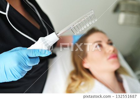 A dermatologist trichologist performs the procedure with a darsonval device to improve the condition and quality of the patient's hair. 132551687