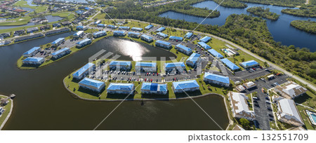 Protective tarp covering rooftop after hurricane damage against rain water leaking until replacement of asphalt shingles on damaged apartment buildings. Aftermath of natural disaster Protective tarp covering rooftop after hurricane damage against rain water leaking until replacement of asphalt shingles on damaged apartment buildings. Aftermath of natural disaster 132551709