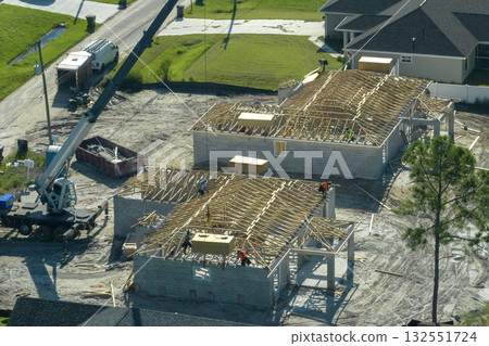 Professional builders and crane truck working on roof construction of unfinished suburban home with wooden frame structure in Florida rural area. Concept of housing development in America Professional builders and crane truck working on roof construction of unfinished suburban home with wooden frame structure in Florida rural area. Concept of housing development in America 132551724