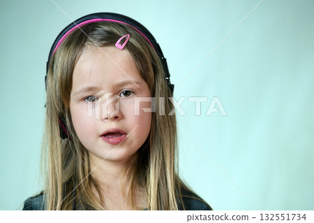 Pretty smiling cild girl listening to music in big pink earphones. 132551734