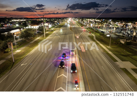 Police vehicle with emergency lights stops a driver for speeding on city road at night in the United States. Traffic moving rapidly on wide highway street. 132551748