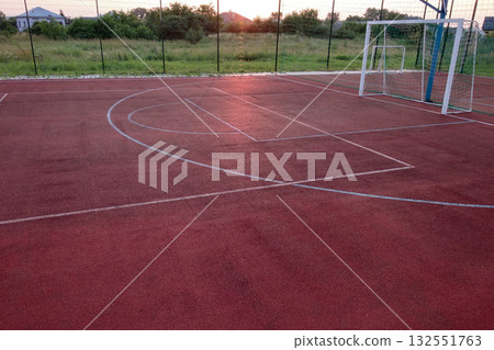 Outdoors mini football and basketball court with ball gate and basket surrounded with high protective fence. Outdoors mini football and basketball court with ball gate and basket surrounded with high protective fence. 132551763