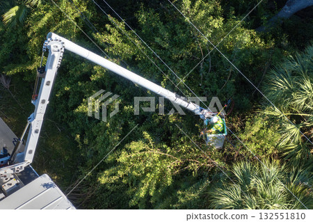 Maintenance of electrical grid by city utility cervices. Worker in lift truck trimming tree around power lines 132551810