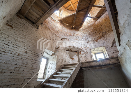 Large spacious forsaken empty basement room of ancient building or palace with cracked plastered brick walls, small windows, dirty floor and wooden staircase ladder. 132551824