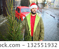 attractive bearded man in santa hat holding a christmas tree in his hands and smiling on the background of a red retro car. 132551932