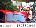 mom, dad in a Santa hat and a daughter in a knitted red hat with pigtails hug and smile against the background of a red car with a Christmas tree on the roof 132551944