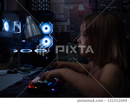 A child plays computer games. A young child is focused on playing a video game on a personal computer, his hands resting on the colorfully backlit keyboard in a dark room. A child plays computer games. A young child is focused on playing a video game on a personal computer, his hands resting on the colorfully backlit keyboard in a dark room. 132552049