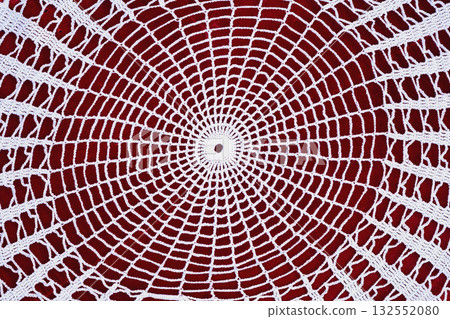 White crochet doily in circular geometric pattern placed on red background. Concept of handmade art, vintage style, traditional style. Craft background 132552080