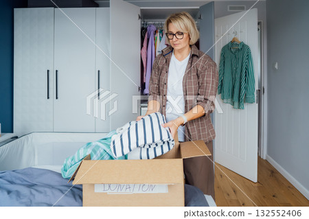 Woman putting selected clothes from her wardrobe for donating to a Charity shop. Decluttering, Sorting clothes and Cleaning Up. Reuse, second-hand concept. Conscious consumer, sustainable lifestyle Woman putting selected clothes from her wardrobe for donating to a Charity shop. Decluttering, Sorting clothes and Cleaning Up. Reuse, second-hand concept. Conscious consumer, sustainable lifestyle 132552406