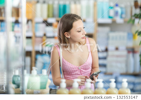 Female shopper searches for necessary goods on the shelves of a supermarket, checking list on her smartphone 132553147