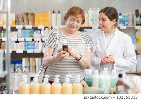 Mature woman choosing syrup on the recommendation of a pharmacist Mature woman choosing syrup on the recommendation of a pharmacist 132553318