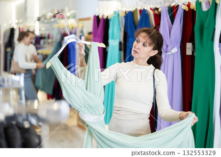 Middle-aged woman girl choosing party dress in clothing store Middle-aged woman girl choosing party dress in clothing store 132553329