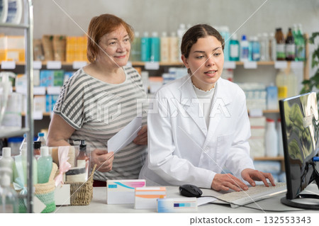 Female pharmacist counseling mature woman near cash register in pharmacy Female pharmacist counseling mature woman near cash register in pharmacy 132553343