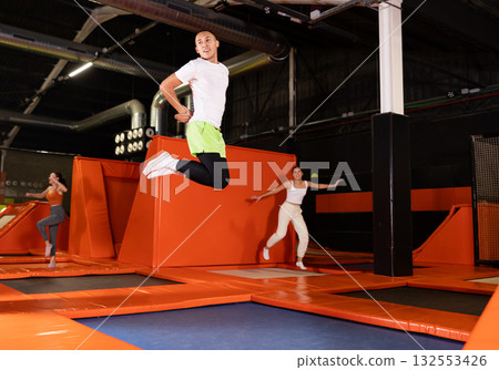 Cheerful young man jumping in modern indoor trampoline park 132553426