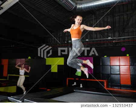 Enthusiastic woman leaping at vibrant trampoline gym with friends Enthusiastic woman leaping at vibrant trampoline gym with friends 132553437