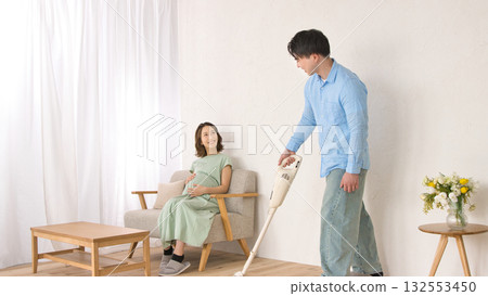 一位年輕男子一邊愉快地吸塵,一邊和孕婦聊天。 一位年輕男子一邊愉快地吸塵,一邊和孕婦聊天。 132553450