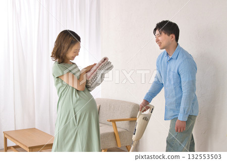 一位年輕男子一邊用吸塵器打掃衛生,一邊和一位孕婦愉快地聊天。 一位年輕男子一邊用吸塵器打掃衛生,一邊和一位孕婦愉快地聊天。 132553503