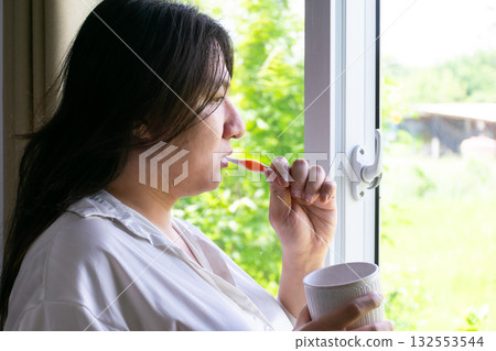 Thai LGBTQ person brushing teeth by the window in morning light showing natural lifestyle calm mood and real selfcare moment in everyday life 132553544