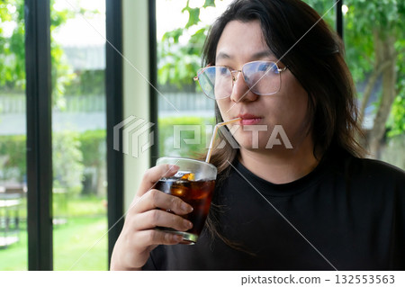 Thai LGBTQ person enjoying a cold drink while waiting for lunch in a cozy restaurant with warm daylight showing calm happiness and real lifestyle moments Thai LGBTQ person enjoying a cold drink while waiting for lunch in a cozy restaurant with warm daylight showing calm happiness and real lifestyle moments 132553563