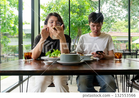 Two Thai LGBTQ friends enjoying lunch together sharing food photos and chatting online in a cozy bright cafe showing friendship connection and real lifestyle moments Two Thai LGBTQ friends enjoying lunch together sharing food photos and chatting online in a cozy bright cafe showing friendship connection and real lifestyle moments 132553566