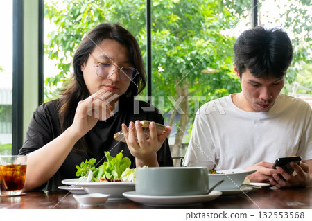 Two Thai LGBTQ friends enjoying lunch together scrolling through phones sharing moments online in cozy daylight cafe showing friendship connection and real lifestyle happiness 132553568