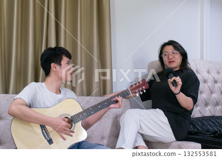 Two Thai LGBTQ friends spending a warm afternoon together playing guitar and singing at home showing friendship creativity and relaxed lifestyle 132553581