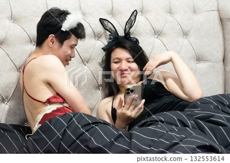 Two Thai LGBTQ friends relaxing on bed checking stock prices and social media laughing and enjoying evening together in cozy bedroom lifestyle moment Two Thai LGBTQ friends relaxing on bed checking stock prices and social media laughing and enjoying evening together in cozy bedroom lifestyle moment 132553614
