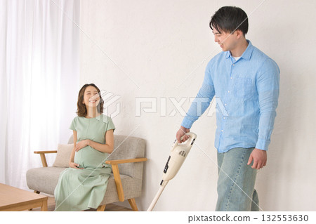 A young man vacuuming happily while talking to a pregnant woman A young man vacuuming happily while talking to a pregnant woman 132553630