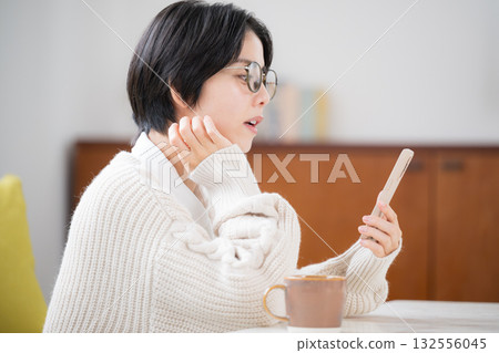 房間裡，一位身穿針織衫的女子側臉看著她的智慧型手機，臉上帶著擔憂和困惑的表情。 132556045