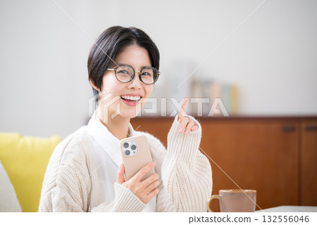 一位短髮女子身穿針織衫,在房間裡低頭擺弄著智慧型手機。可愛的袖子和尖角設計是亮點。 一位短髮女子身穿針織衫,在房間裡低頭擺弄著智慧型手機。可愛的袖子和尖角設計是亮點。 132556046