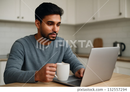 AI generated young South Asian man working from home in his kitchen with a cup of coffee. The minimalist space is lit with natural light creating a focused atmosphere perfect for remote work. 132557294