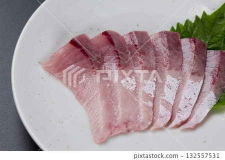 盛在盤子裡的黃尾魚刺身，背景是黑色。 132557531