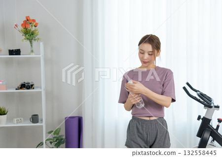 Young woman people engaged in home fitness activity, taking break for essential hydration with water bottle, promoting healthy active lifestyle, displaying commitment to personal wellness 132558445