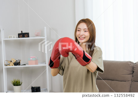 Young happy woman enjoys activity at home, engaging in fitness training workout, wearing red boxing gloves, people embracing active lifestyle, finding joy in personal exercise 132558492