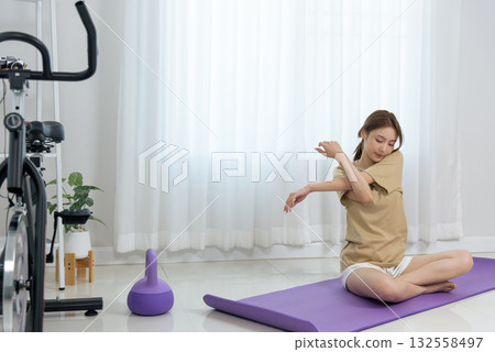 Young woman stretching arm, engaging in home activity on yoga mat, practicing gentle exercise, promoting healthy people lifestyle, happy and focused for wellness Young woman stretching arm, engaging in home activity on yoga mat, practicing gentle exercise, promoting healthy people lifestyle, happy and focused for wellness 132558497
