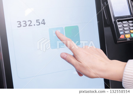 A woman uses her finger to choose a payment method on a touchscreen display during a self-service transaction. self-service at the checkout in the store via the touchscreen screen A woman uses her finger to choose a payment method on a touchscreen display during a self-service transaction. self-service at the checkout in the store via the touchscreen screen 132558554