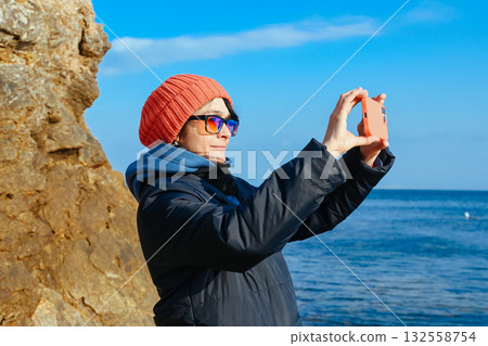 Russian woman photographing the Sea of Japan coast in Vladivostok during a cold sunny day. Travel blogger capturing scenic ocean view and inspiration. Russian woman photographing the Sea of Japan coast in Vladivostok during a cold sunny day. Travel blogger capturing scenic ocean view and inspiration. 132558754