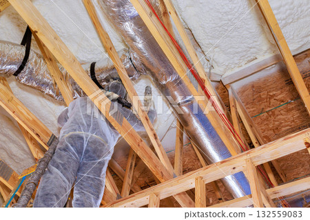 Construction worker is busy installing ductwork inside new home under construction, working on ceiling supports. Construction worker is busy installing ductwork inside new home under construction, working on ceiling supports. 132559083