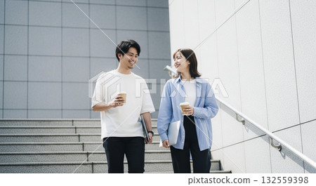 一對年輕男女手捧咖啡,走下樓梯。 一對年輕男女手捧咖啡,走下樓梯。 132559398