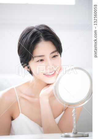 A beautiful woman with short black hair checking her skin care in the mirror. Image of beauty, beauty, and beautiful skin. 132560058