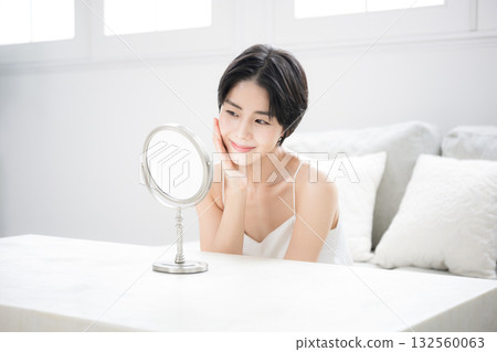 A beautiful woman with short black hair checking her skin care in the mirror. Image of beauty, beauty, and beautiful skin. 132560063