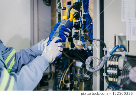 Electrician engineer worker testing electric cable at main power line cabinet fuse box. 132560336
