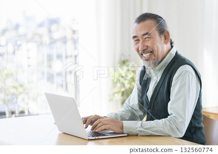 A man in his 70s working on a laptop, smiling and looking at the camera A man in his 70s working on a laptop, smiling and looking at the camera 132560774